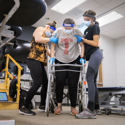 Two occupational students assist another using a walker