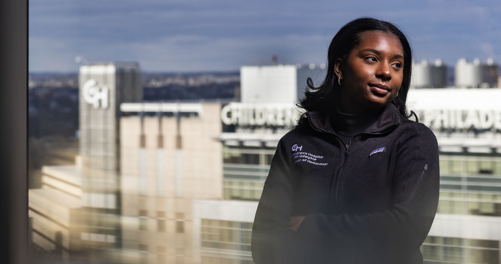 Alumna Deja Houser stands on a rooftop with Children's Hospital of Philadelphia visible behind her