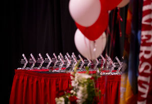an array of diamond-shaped Diamond Awards on a table with a cherry tablecloth, with balloons and flowers in the foreground