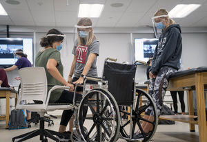 two OT students help one student move from a chair to a wheelchair