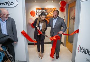 a woman holding large red scissors cuts a ribbon to the new sensory-friendly room in the Social Service Annex
