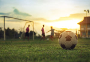 a soccer ball on a field with a group of soccer players out of focus in the distance