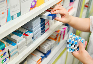 a pharmacist chooses from a wall of prescription drugs