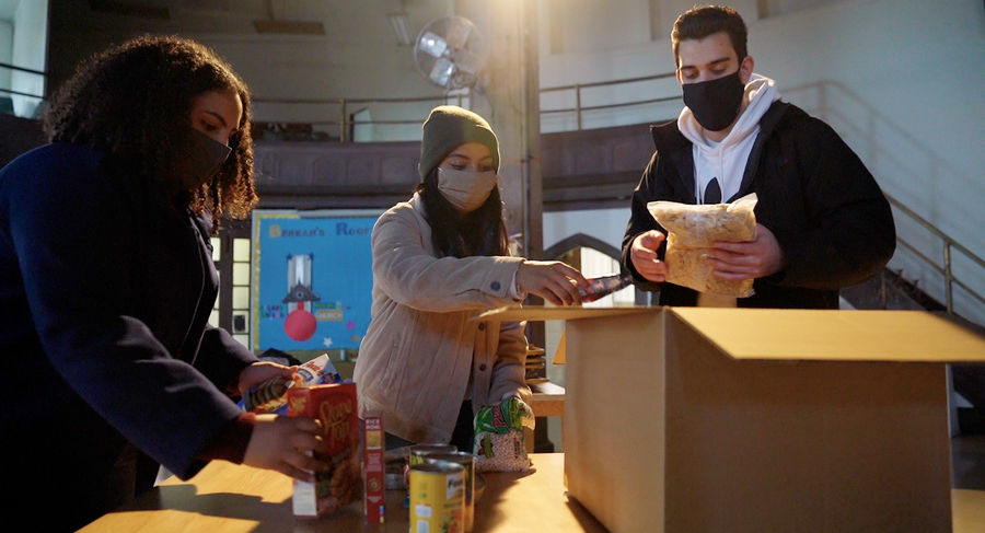 Three students pack cardboard boxes with stuffing, pancake mix and grains