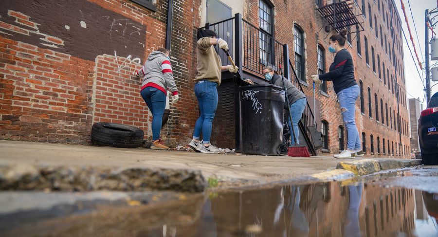 Four volunteers sweep trash into an outdoor trashcan