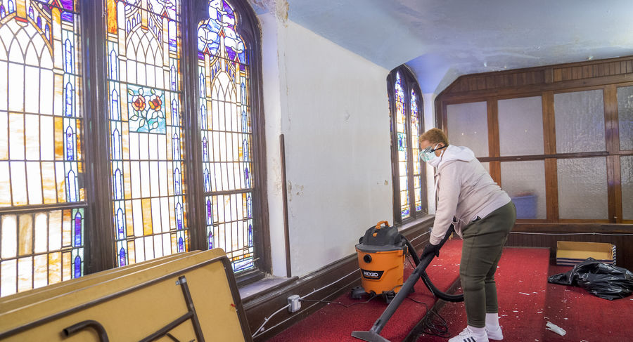 Woman vacuuming carpet in front of stained glass window inside church