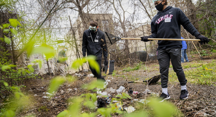Two people rake up debris in a yard