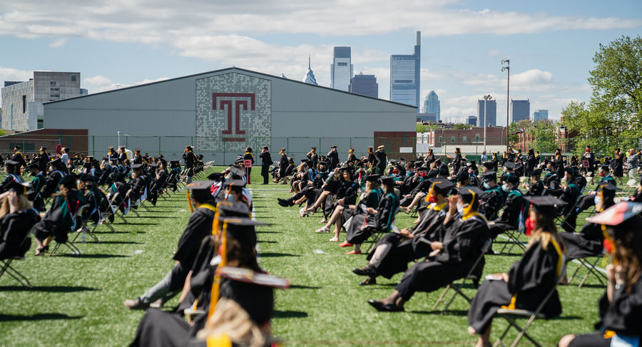 students in caps and gowns line up on geasey field, with philadelphia skyline behind them
