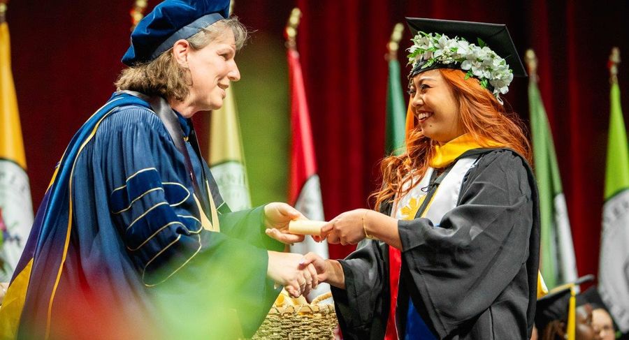 Dean Jennifer Ibrahim hands a scroll to a graduating student.