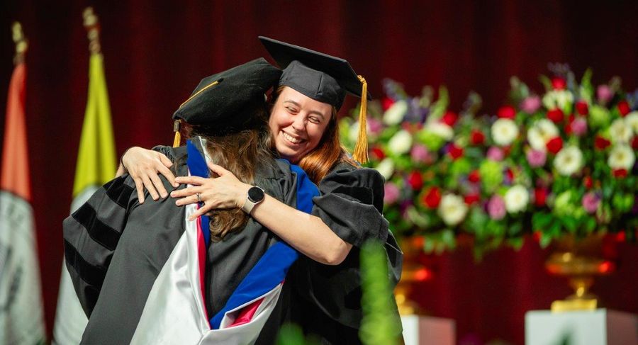 A doctoral student hugs a faculty member on the graduation stage.