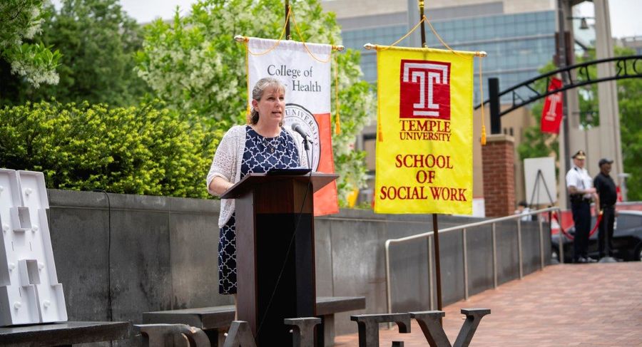 Dean Jennifer Ibrahim speaking at a podium in front of flags for the College of Public Health and the School of Social Work. In front of the podium is the word PALEY in decorative letters.