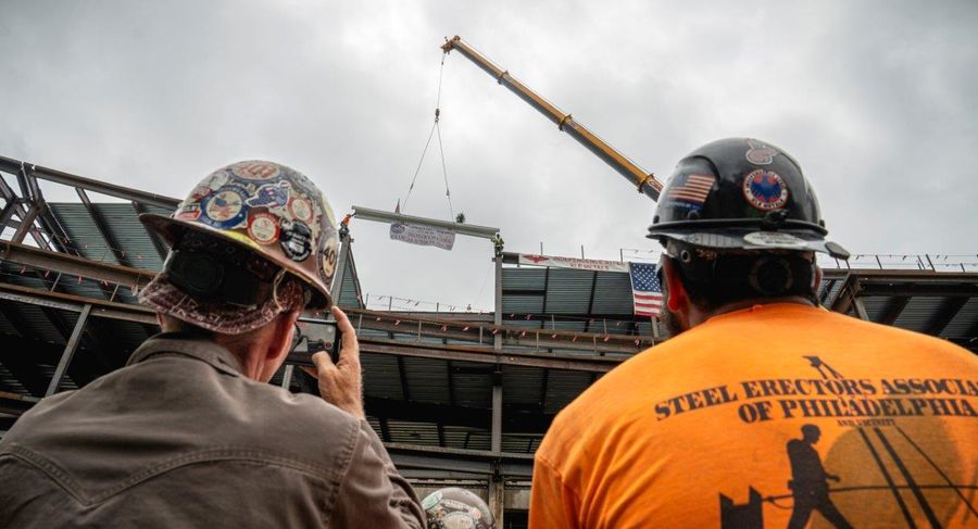 Two construction workers watch the beam being placed into the top of Paley Hall. 