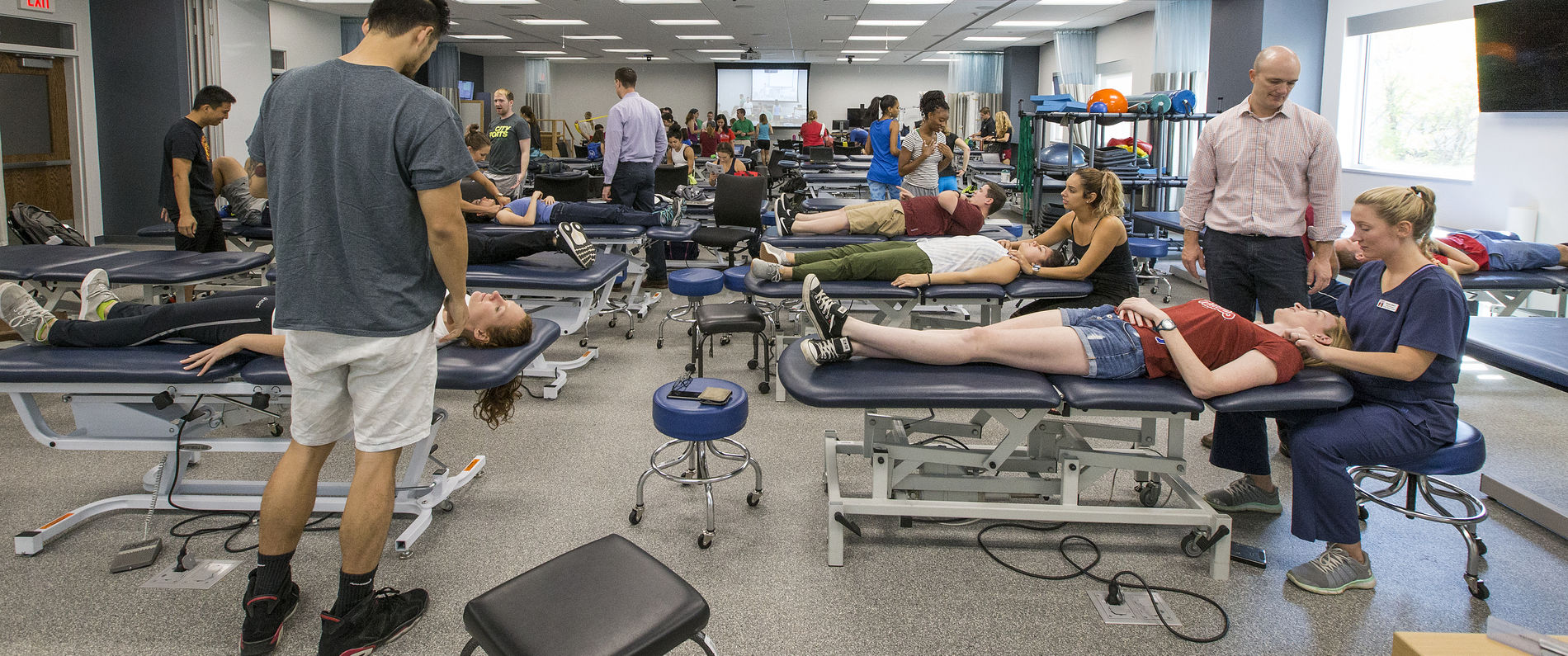 Physical therapy students examining patients on tables