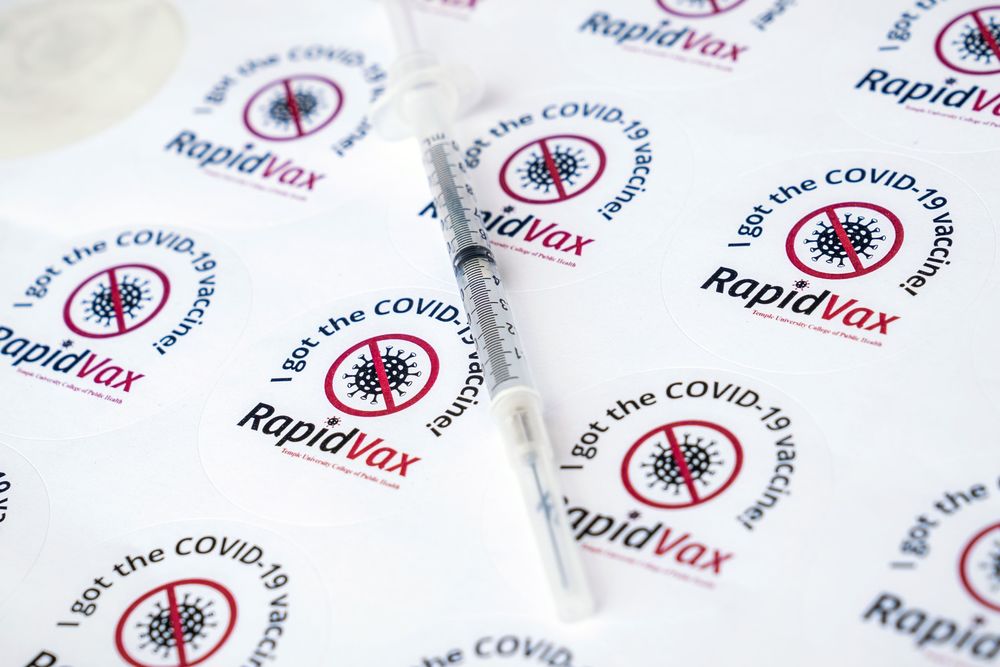 a sheet of stickers bearing the rapidvax logo, with a vaccine needle placed on top