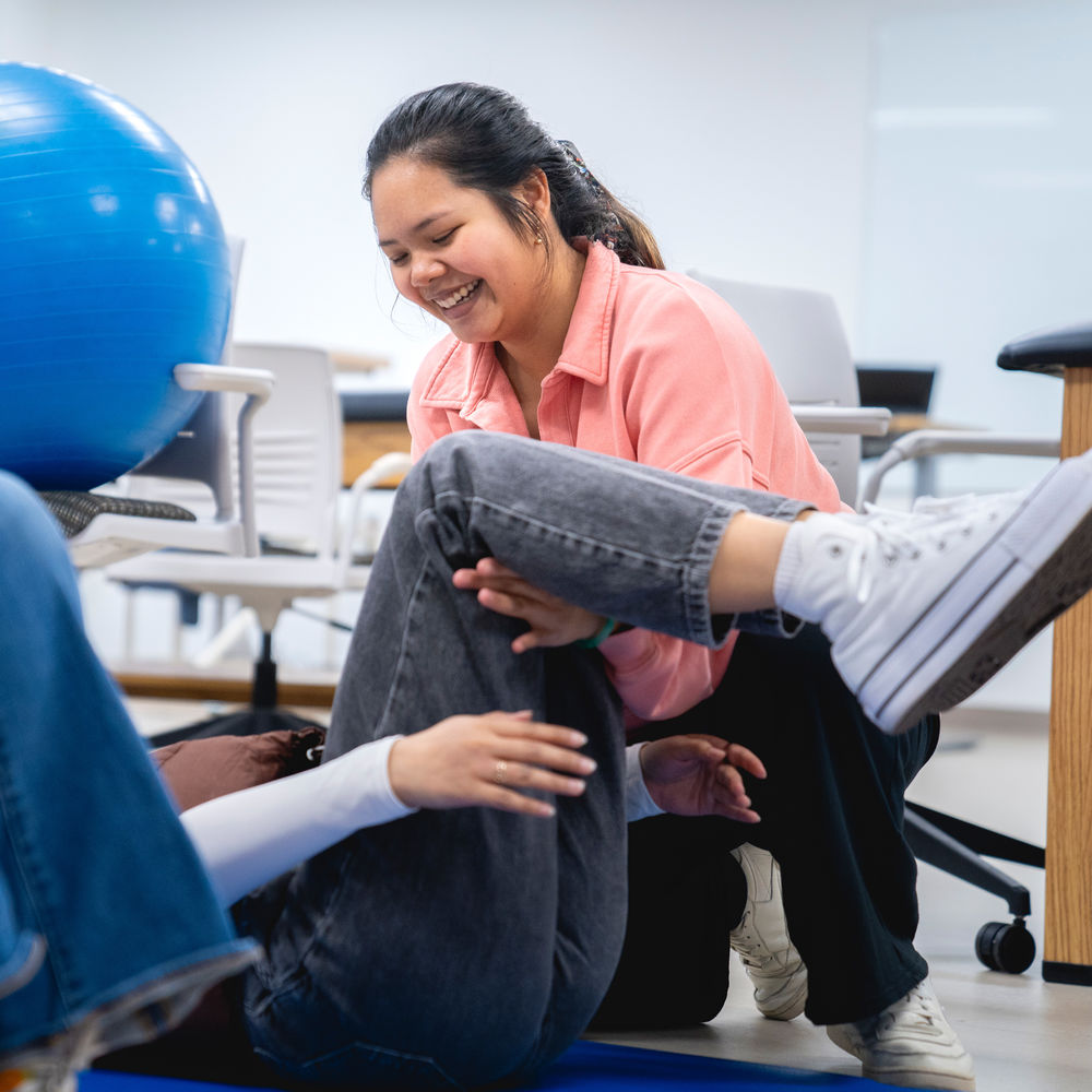 An occupational therapy student lifts a fellow student's leg