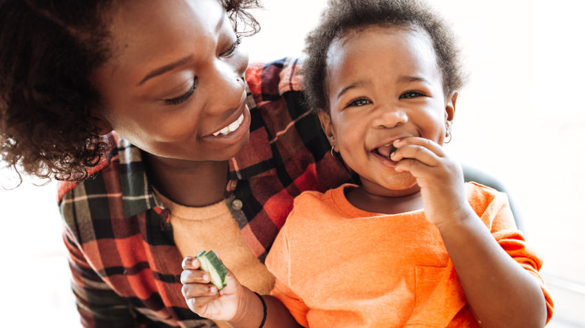 woman holding baby eating a cucumber