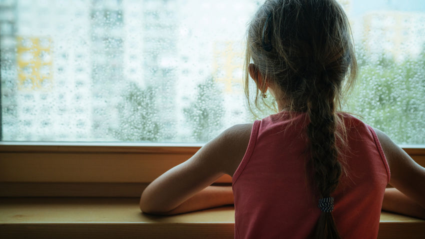 a young girl looks out a rainy window