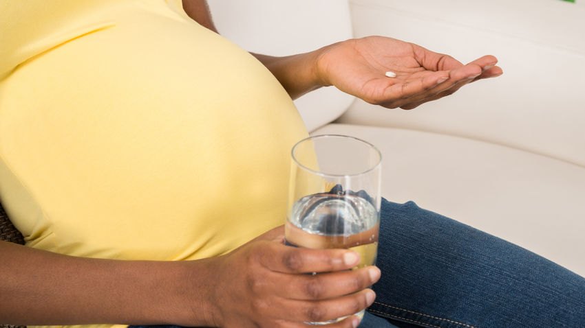 pregnant woman holding a pill and a glass of water