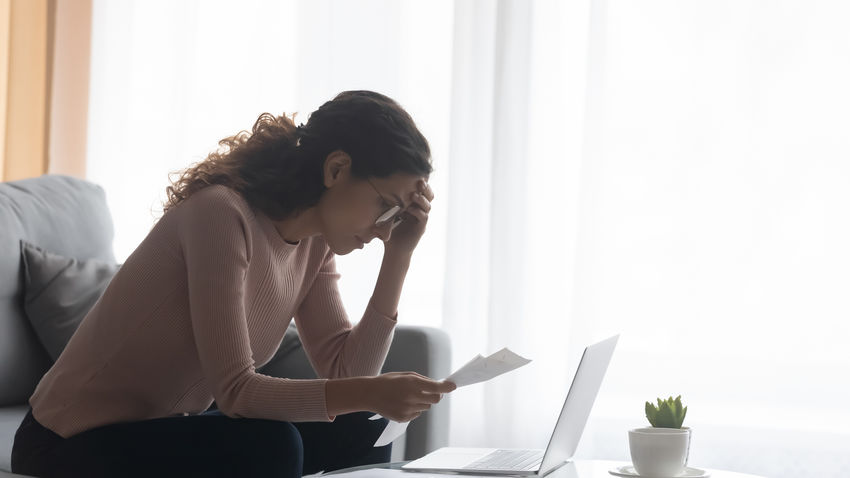 a woman looks at a piece of paper with her head down, holding her hand to her head