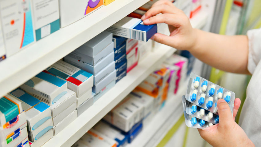 a pharmacist chooses from a wall of prescription drugs