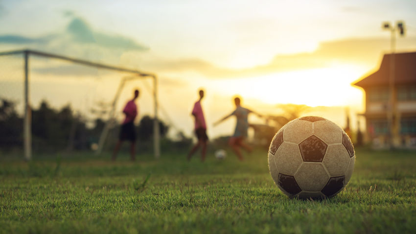 a soccer ball on a field with a group of soccer players out of focus in the distance