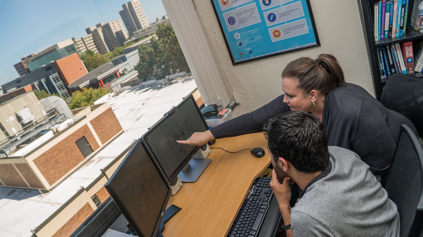 a woman points to a computer screen with 3d data models on it. 