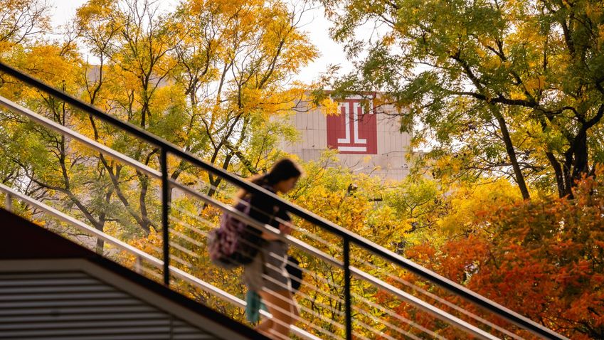 a girl descending stairs on temples campus, with yellow-colored fall foliage in the background next to a Temple T on a building.