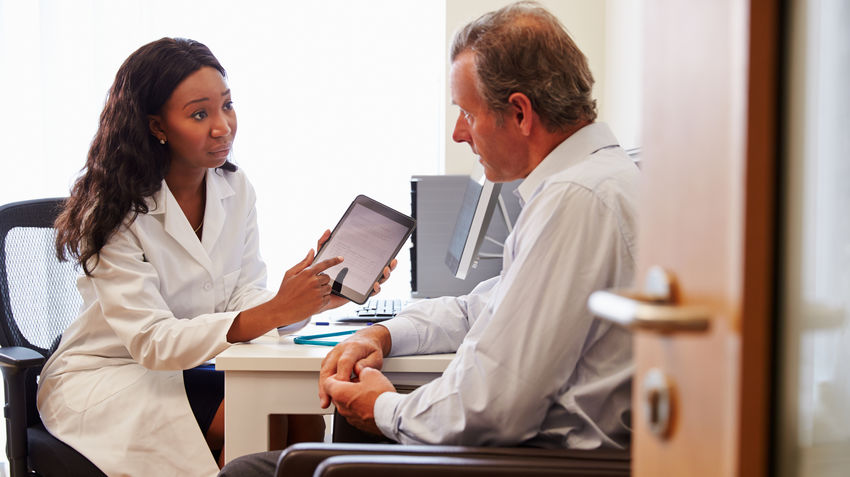 A clinician working with a patient points at a handheld tablet