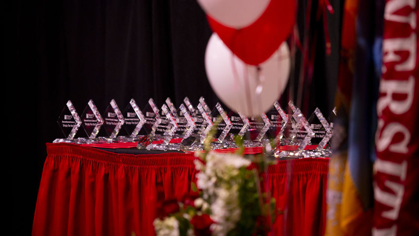 an array of diamond-shaped Diamond Awards on a table with a cherry tablecloth, with balloons and flowers in the foreground
