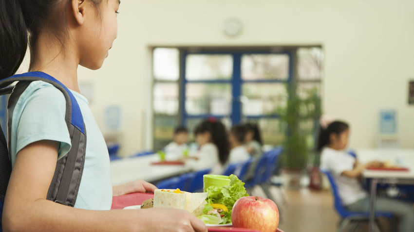 a young student carries a tray of food in a school cafeteria