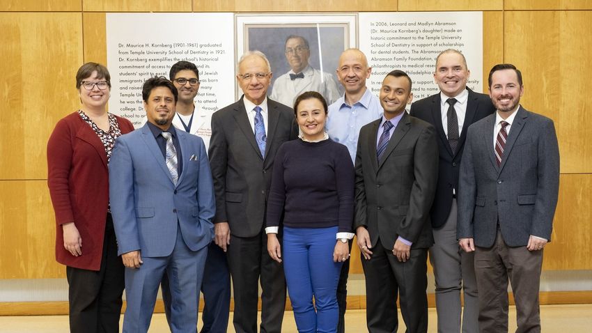 Members of the Kornberg School of Dentistry, the College of Public Health, and the Lewis Katz School of Medicine posing for a photo in front of a photo of Dr. Maurice Kornberg. 
