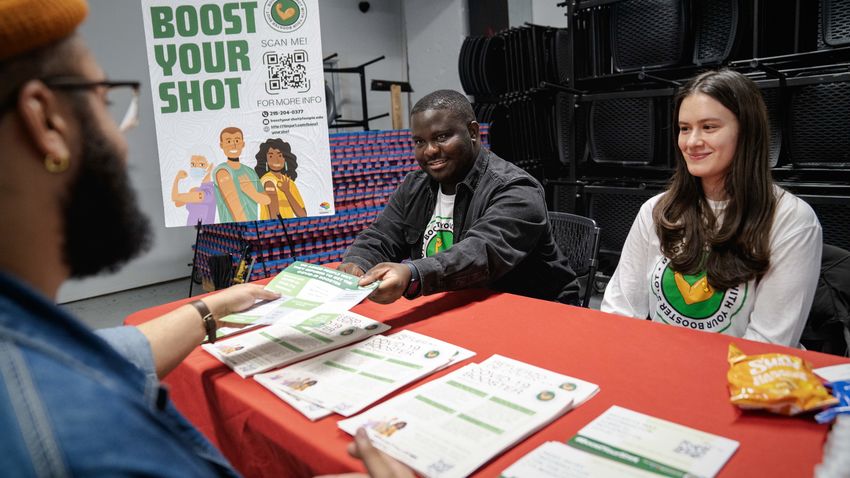 Undergraduate student workers Omari Coker and Molly Piacentini speak with a community member at the Boost Your Shot event at Kensington's Rock Ministries. 