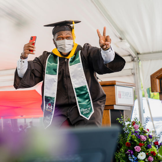 a smiling student makes a peace sign as he crosses the stage at graduation