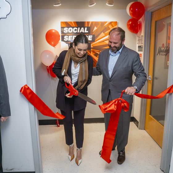 a woman holding large red scissors cuts a ribbon to the new sensory-friendly room in the Social Service Annex