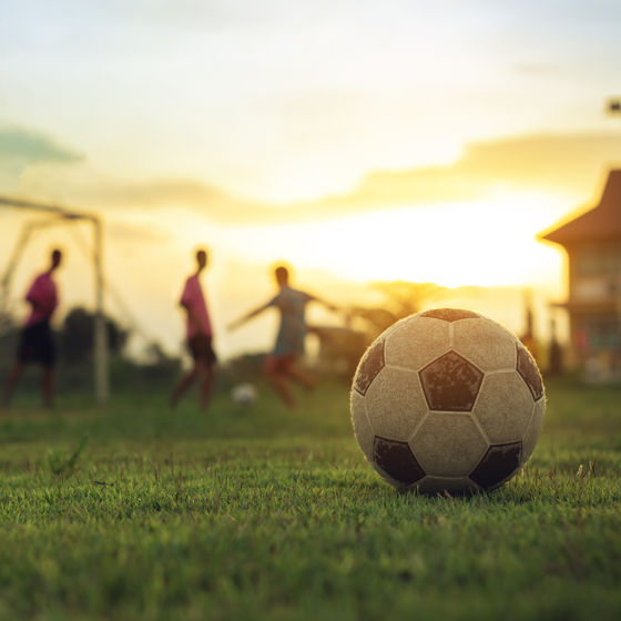 a soccer ball on a field with a group of soccer players out of focus in the distance