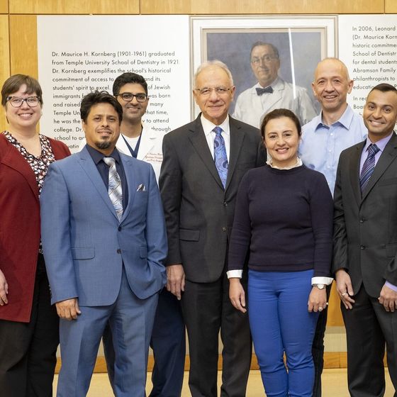 Members of the Kornberg School of Dentistry, the College of Public Health, and the Lewis Katz School of Medicine posing for a photo in front of a photo of Dr. Maurice Kornberg. 