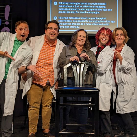 Sarah Bass standing with a group of comedians on a stage at a recent science-themed improv show